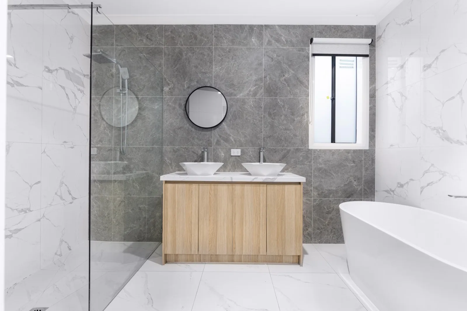 Contemporary bathroom with a wood vanity, tiled walls and freestanding bath.