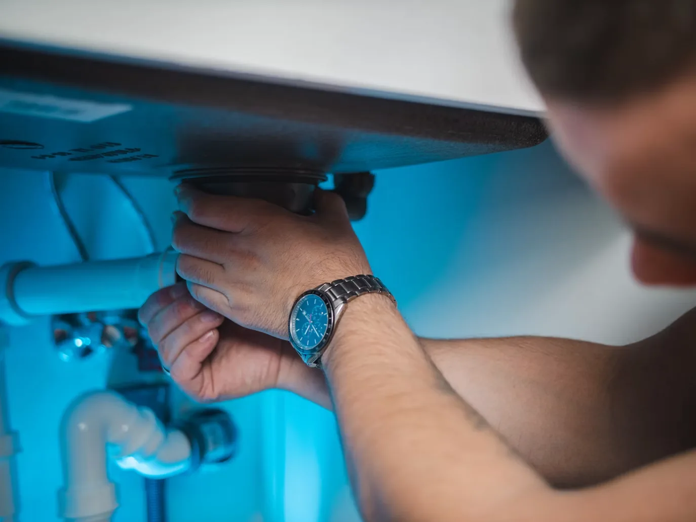 Hands adjusting a kitchen sink drain connection beneath the basin.